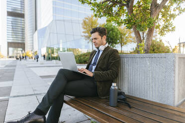 Businessman sitting on bench in the city using laptop, Madrid, Spain - KIJF02755