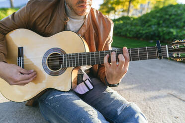 Nahaufnahme eines Gitarre spielenden Mannes in einem Park - KIJF02766