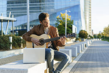 Mann mit Laptop spielt Gitarre in der Stadt, Madrid, Spanien - KIJF02768