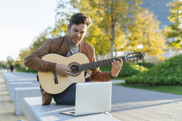 Man with laptop playing guitar in the city, Madrid, Spain - KIJF02769