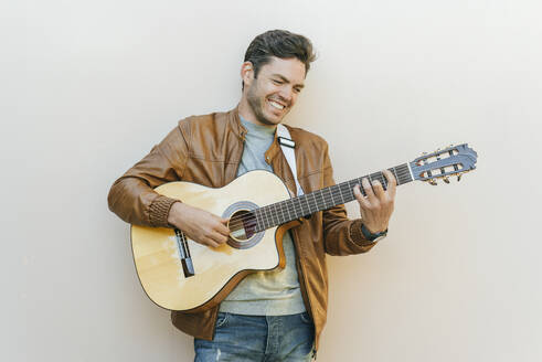 Lächelnder Mann spielt Gitarre vor einer Wand - KIJF02772
