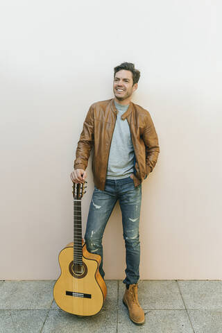 Lächelnder Mann mit Gitarre vor einer Mauer, lizenzfreies Stockfoto