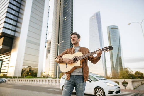 Lächelnder Mann spielt Gitarre in der Stadt, Madrid, Spanien - KIJF02789