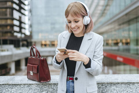 Lächelnde Frau mit Smartphone und Kopfhörern in der Stadt, lizenzfreies Stockfoto
