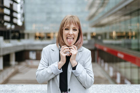 Porträt einer Frau, die ihre Zunge in der Stadt herausstreckt, lizenzfreies Stockfoto