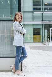 Smiling busineswoman leaning against glass building - KIJF02816