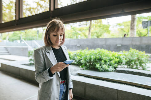 Geschäftsfrau schaut auf Handy im Freien - KIJF02825