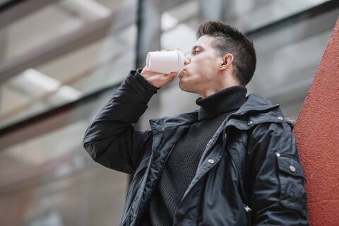 Junger Mann trinkt Kaffee zum Mitnehmen in der Stadt, lizenzfreies Stockfoto