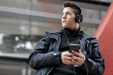 Junger Mann mit Smartphone und Kopfhörern beim Musikhören - DHCF00199