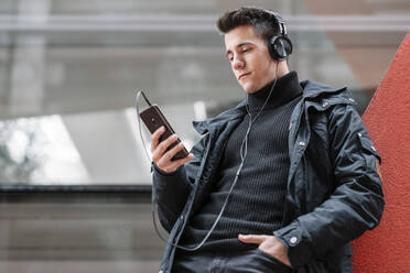 Junger Mann mit Smartphone und Kopfhörern beim Musikhören - DHCF00200