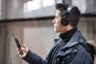 Junger Mann mit Smartphone und Kopfhörern beim Musikhören - DHCF00201