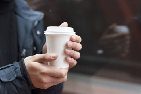 Junger Mann hält einen Kaffee zum Mitnehmen im Freien - DHCF00202