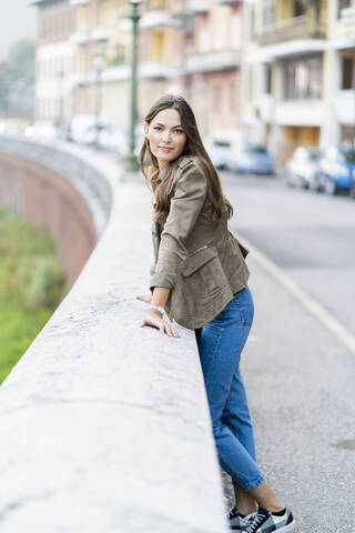 Junge brünette Frau schaut in die Kamera und lehnt sich an eine Wand, lizenzfreies Stockfoto