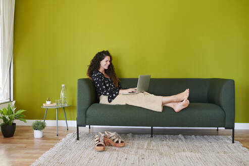 Smiling young businesswoman using laptop on couch in modern office - IGGF01477