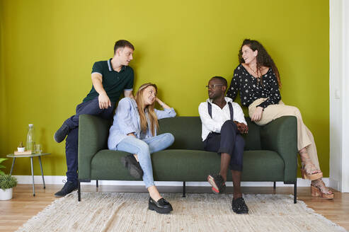 Casual colleagues talking on a sofa in a green walled office lounge - IGGF01478