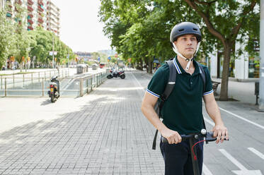 Lässiger junger Geschäftsmann fährt E-Scooter auf dem Fahrradweg in der Stadt - IGGF01490