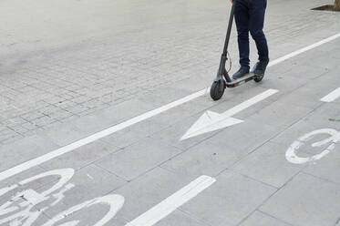 Beine eines Mannes, der einen E-Scooter auf dem Fahrradweg in der Stadt fährt - IGGF01491