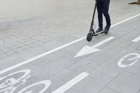 Beine eines Mannes, der einen E-Scooter auf dem Fahrradweg in der Stadt fährt - IGGF01491