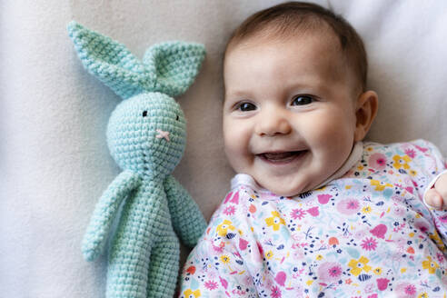 Baby girl with a stuffed bunny toy lying on bed - GEMF03305