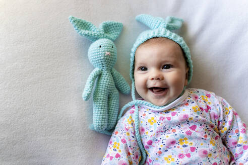 Baby-Mädchen mit Hasenmütze und einem Hasen-Spielzeug auf dem Bett liegend - GEMF03307