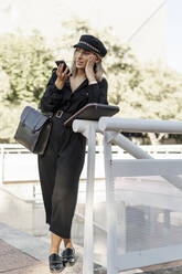 Junge blonde Geschäftsfrau mit schwarzem Hut und Smartphone - ERRF02080