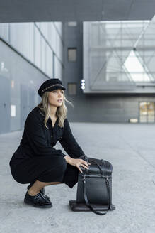 Junge blonde Geschäftsfrau mit Matrosenmütze, die in ihrer Tasche sucht - ERRF02096