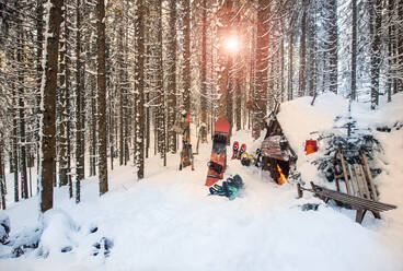 Österreich, Salzburg, Altenmarkt im Pongau, Wintersportgeräte liegen vor einer verschneiten Waldhütte bei Sonnenuntergang - HHF05574
