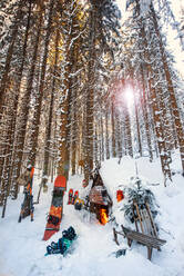 Austria, Salzburg, Altenmarkt im Pongau, Winter sports equipment lying in front of snow-covered forest hut at sunset - HHF05575