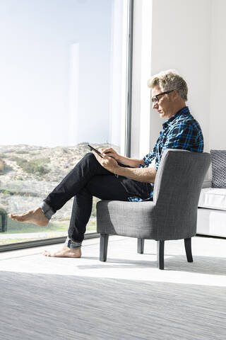 Lässiger Geschäftsmann, der in einem modernen Haus sitzt und ein Tablet benutzt, lizenzfreies Stockfoto