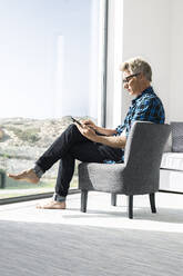Lässiger Geschäftsmann, der in einem modernen Haus sitzt und ein Tablet benutzt - SBOF02035