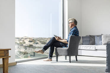 Casual businessman sitting in modern home using tablet - SBOF02036