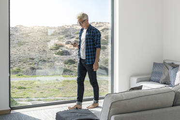 Casual businessman in front of window in modern home holding smartphone - SBOF02040