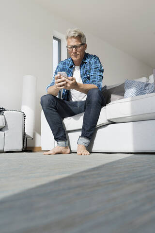 Lässiger Geschäftsmann, der in einem modernen Haus sitzt und ein Smartphone benutzt, lizenzfreies Stockfoto