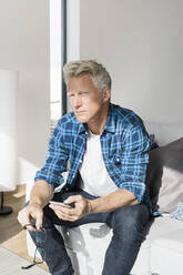 Casual businessman sitting in modern home holding smartphone - SBOF02042