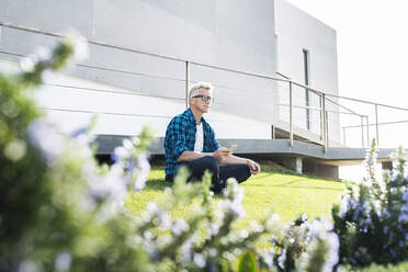 Casual man outside his modern home holding smartphone - SBOF02049