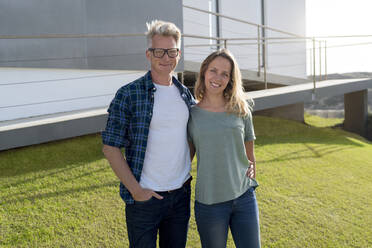 Portrait of smiling couple standing in front of their modern home - SBOF02056