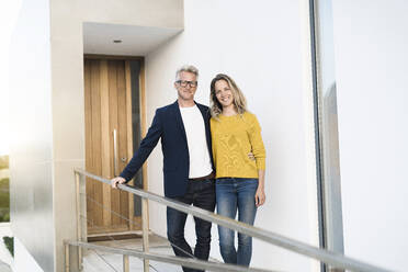 Portrait of smiling couple standing in front of their modern home - SBOF02073