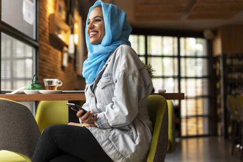 Young woman wearing turquoise hijab and using smartphone in a cafe stock photo