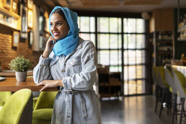 Junge Frau mit türkisfarbenem Hidschab in einem Café - ERRF02143