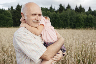 Portrait of senior man in an oat field carrying granddaughter on his arms - EYAF00689