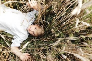 Portrait of blond boy with oat ear in mouth lying in an oat field - EYAF00692