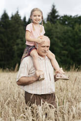 Portrait of happy little girl on grandfather's shoulders in an oat field - EYAF00695