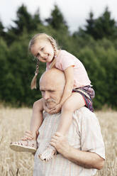 Portrait of happy little girl on grandfather's shoulders in an oat field - EYAF00696