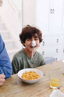 Junge lacht über Löffel, der beim Frühstück auf der Nase klebt - ISF22721