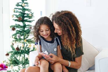 Mother giving daughter present beside Christmas tree at home - ISF22731