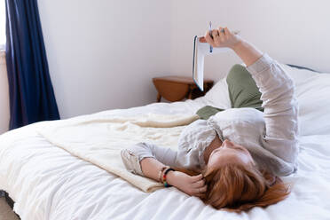 Young woman with red hair reclining on bed reading her diary - ISF22798