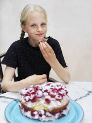 Mädchen isst ihren selbstgebackenen Kuchen mit frischen Himbeeren am Küchentisch, Porträt - CUF53268