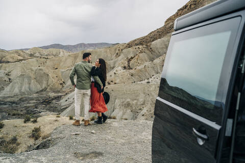 Junges Paar in Wüstenlandschaft unter bewölktem Himmel neben einem Wohnmobil, Almeria, Andalusien, Spanien, lizenzfreies Stockfoto