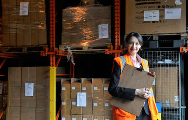 Young female factory worker with clipboard in warehouse, portrait - CUF53451