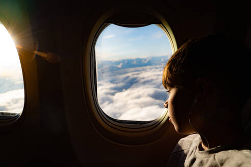 Jugendlicher schaut durch das Flugzeugfenster auf die Wolken im Flugzeug - CUF53529